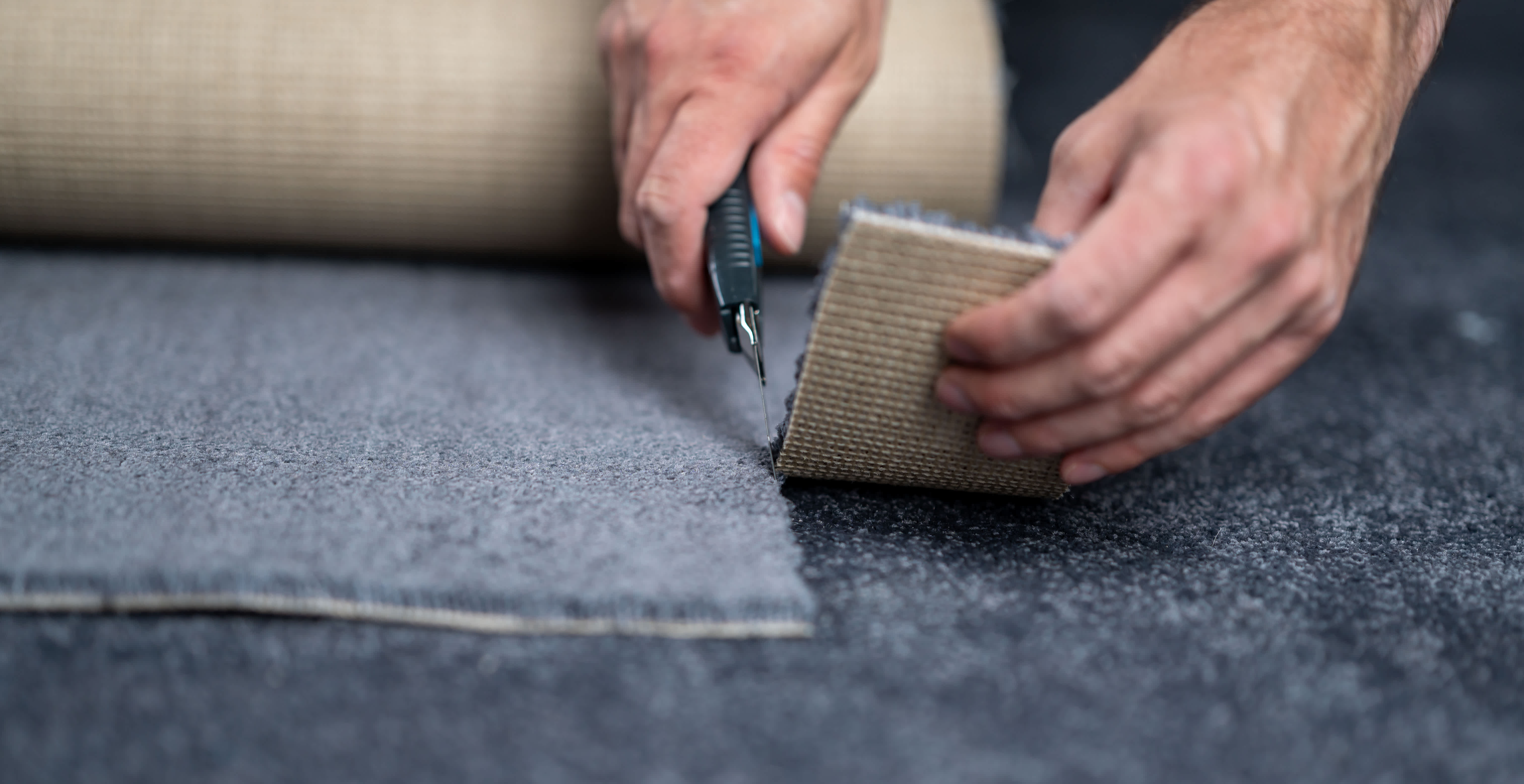 Person carefully cutting a new carpet with a carpet cutter, focusing on precision and technique during carpet installation.