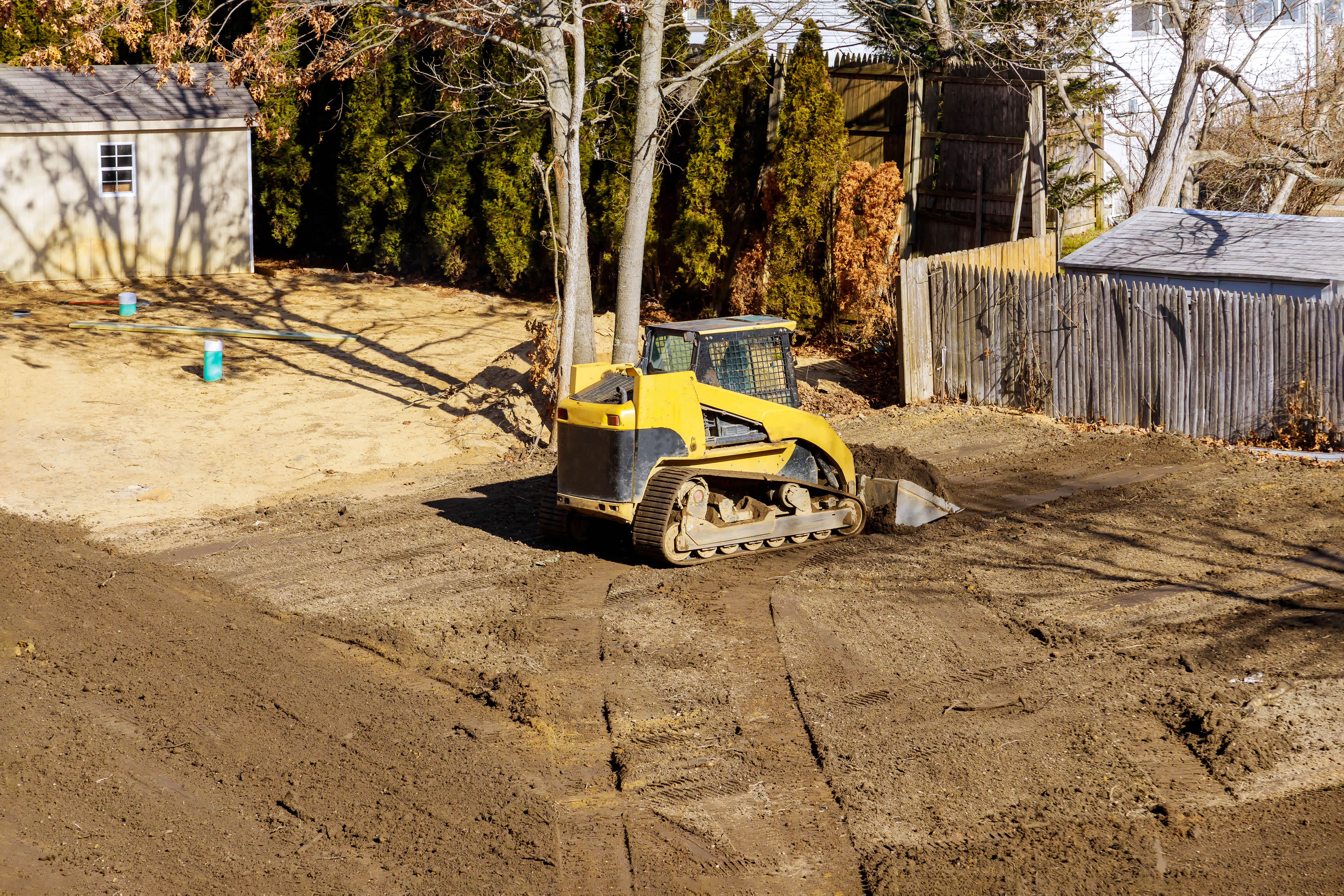 A bulldozer performs major grading and resloping of a house's backyard, leveling the ground during excavation work