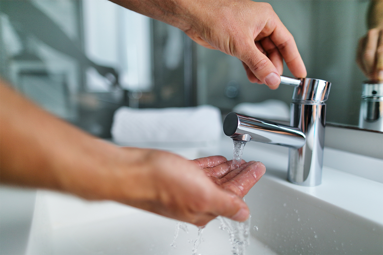A hand lifting a sink faucet and holding hand under stream of water