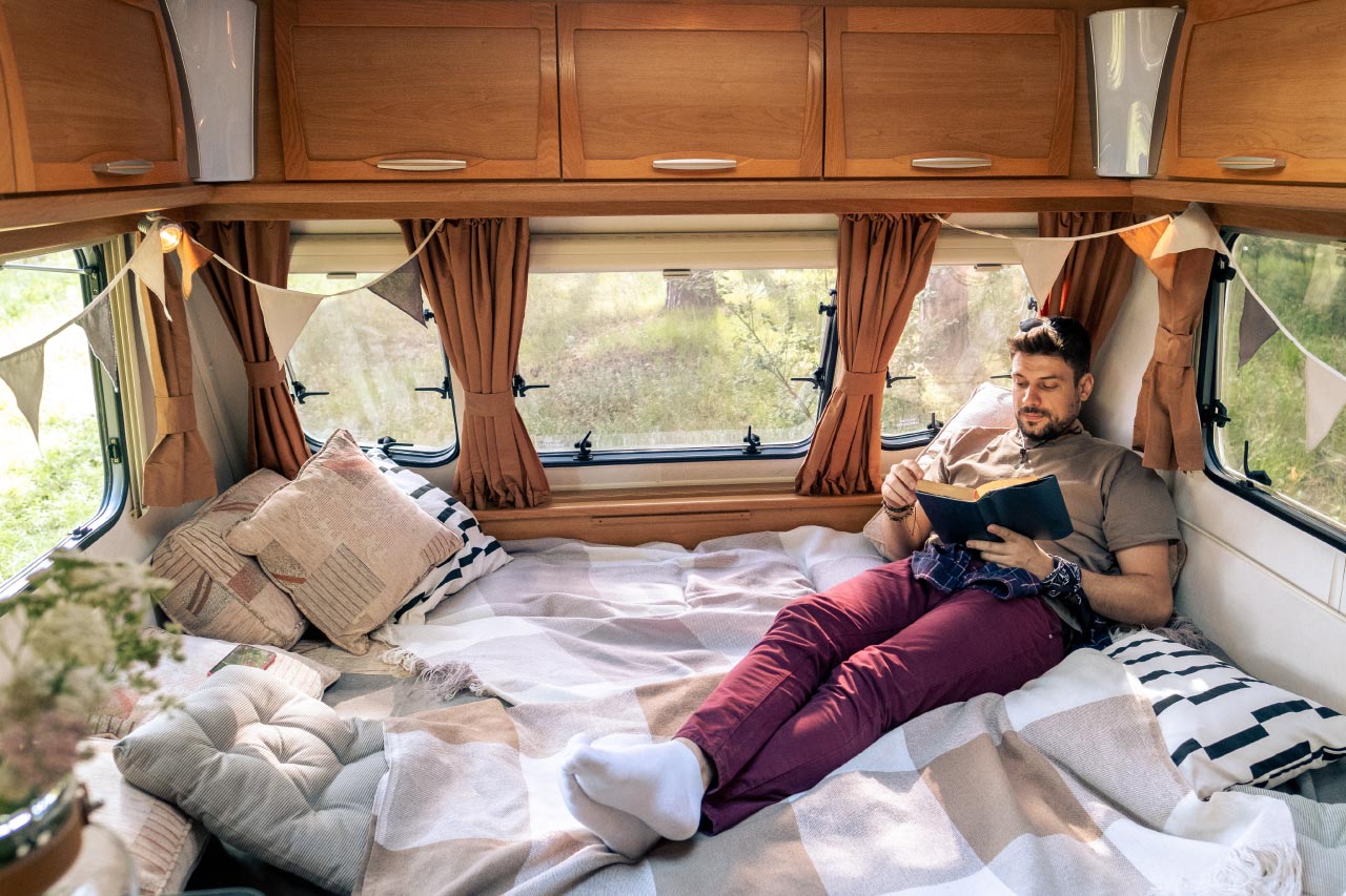 Man reading book while relaxing on bed inside the bus