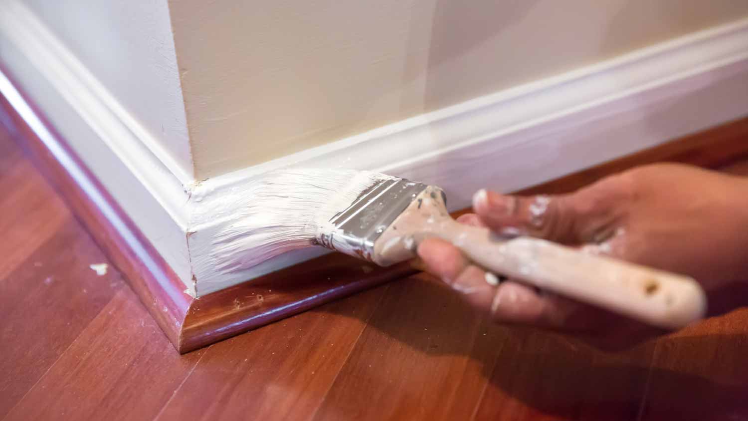 Painter using a paintbrush to paint baseboard