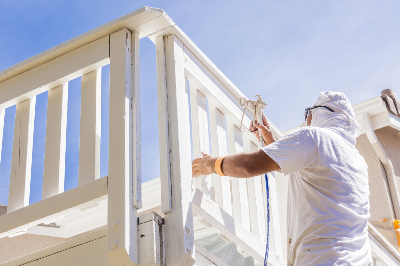 A person in protective gear painting a deck white