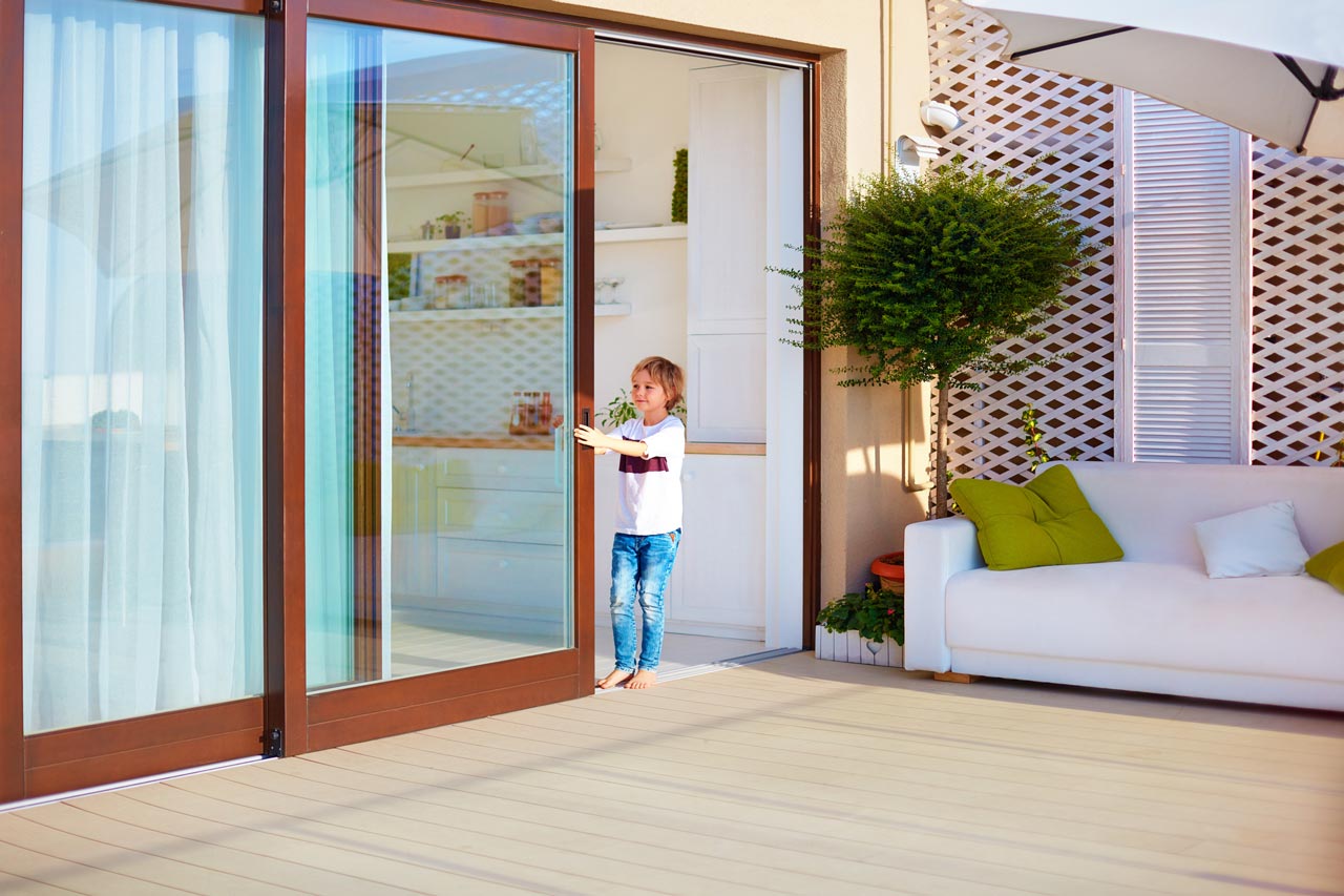 A small boy opening a sliding door leading to a patio