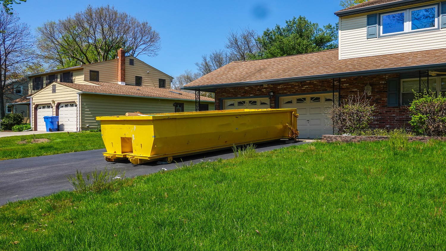 A yellow dumpster in a driveway of a house